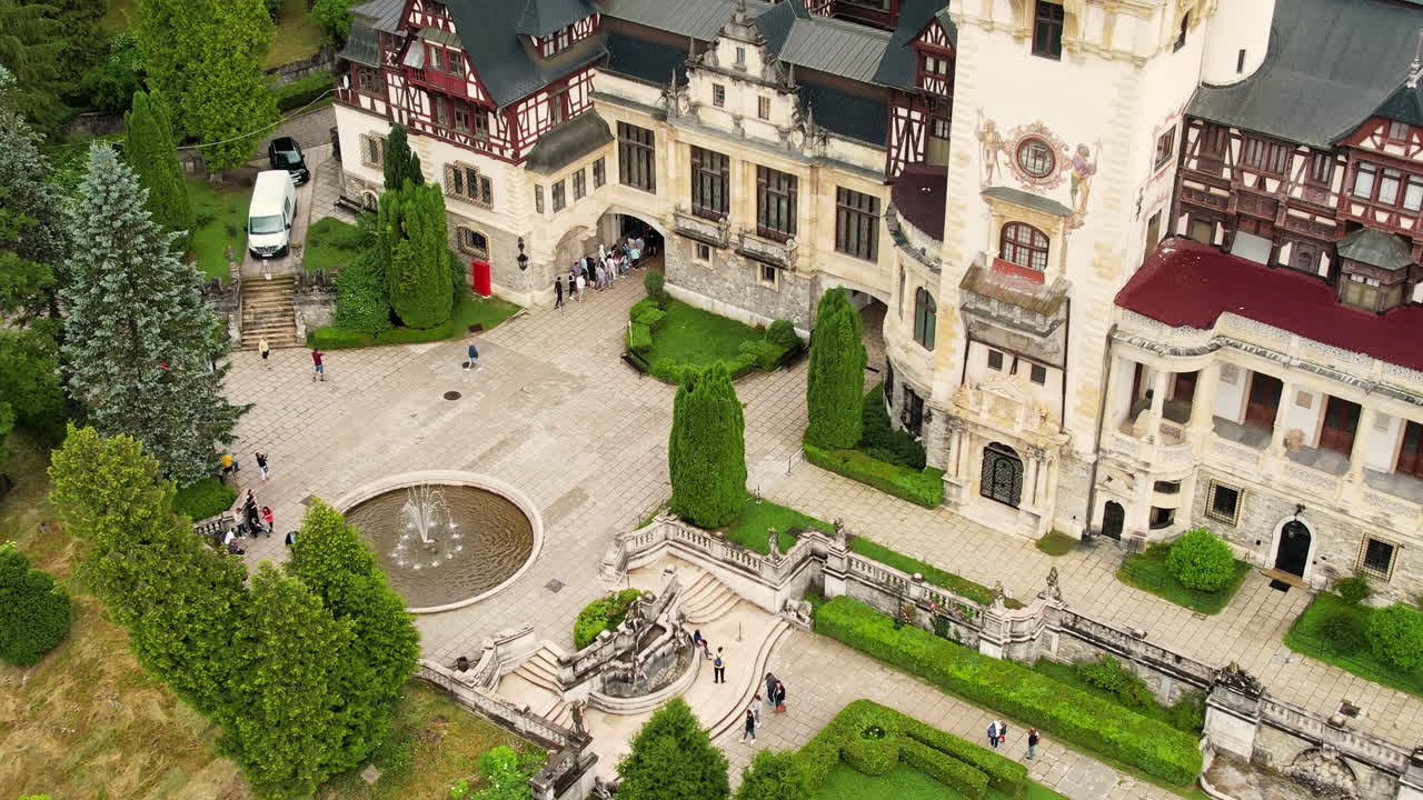 Vista aerea con drone del Castello di Peleș in Romania. Castello con giardini e turisti nei Carpazi, foresta lussureggiante tutt'intorno