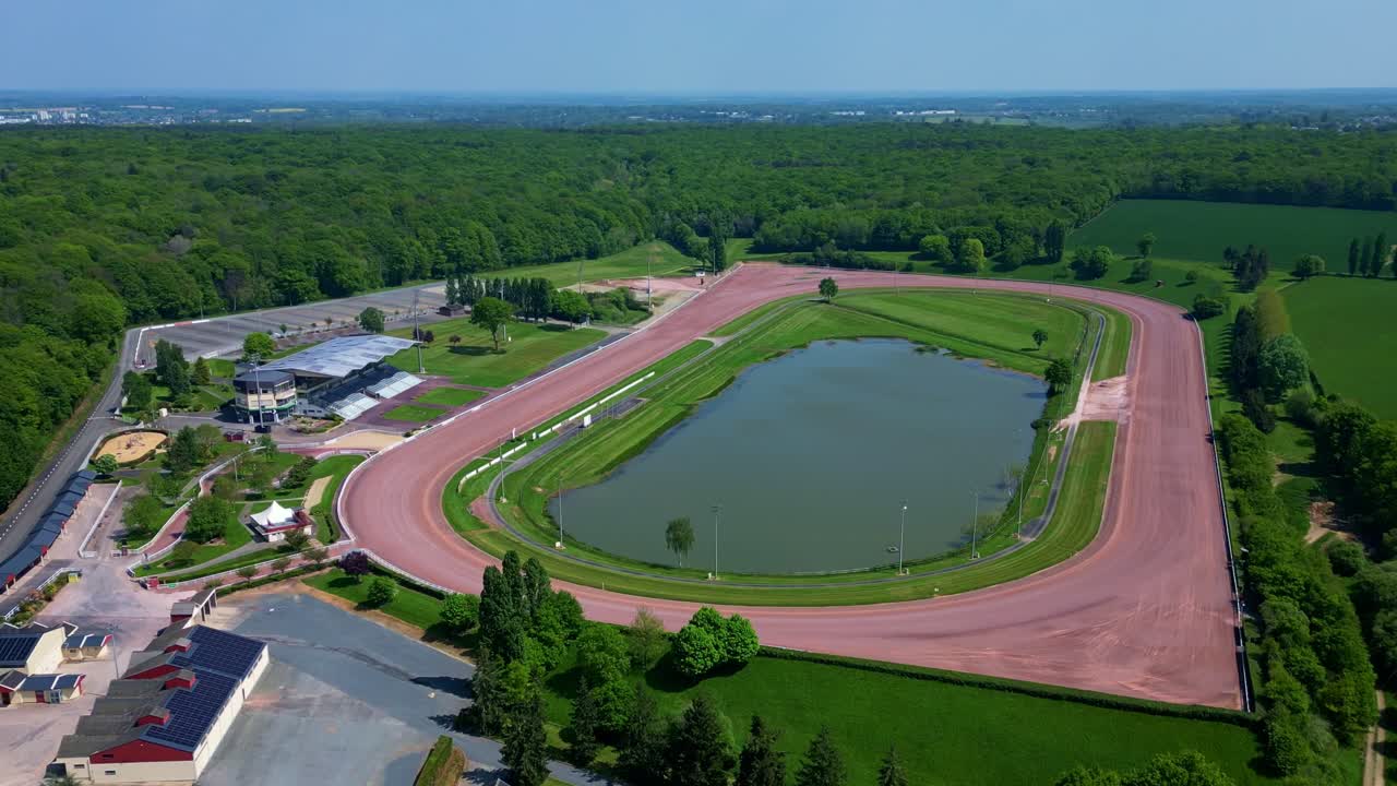 Smooth receding drone movement from the symmetrical hippodrome racecourse surrounded by green forest landscape, Laval, Mayenne, France.