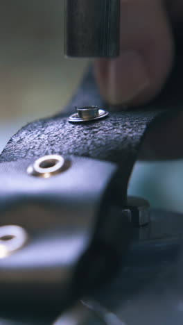 cu: professional designer sets silver eyelets on black leather belt with special press machine closeup