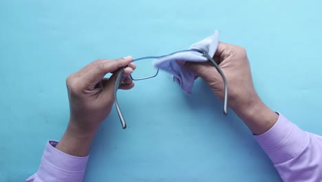 cleaning eyeglass with tissue on blue background top view