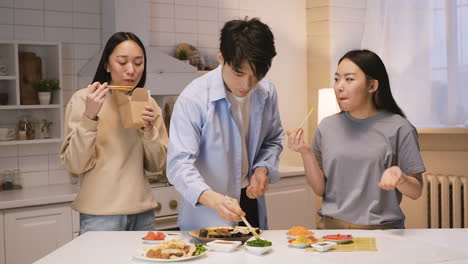 tres amigos japoneses alrededor del mostrador de la cocina y comiendo comida japonesa