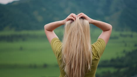 Lady-traveler-adjusts-long-hair-standing-at-mountain-valley