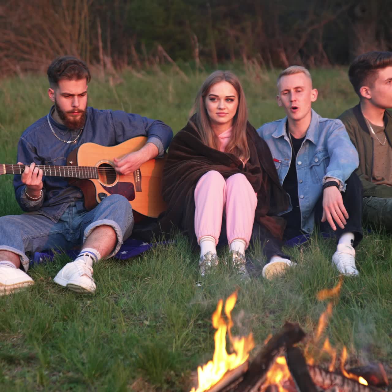 En gruppe venner nyder en sommeraften i naturen. Unge mænd spiller musik og synger sange. Vennerne sidder omkring lejrbålet.