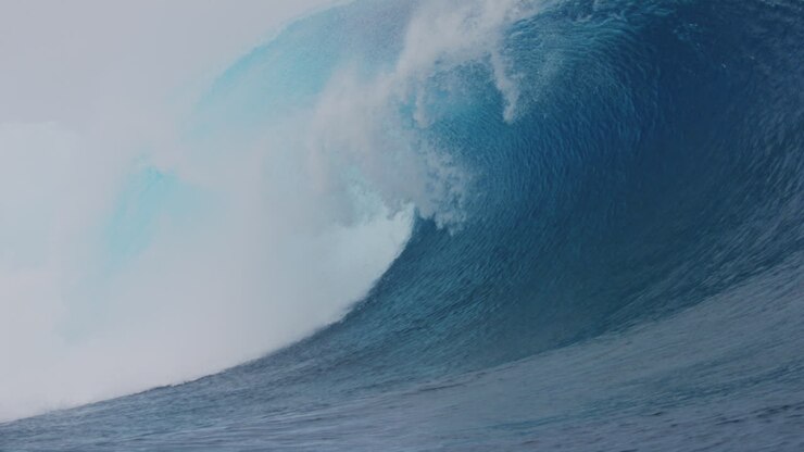 Slow motion barreling wave with crystal clear blue turquoise texture and wind spray whitewash