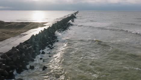 aerial establishing view of port of liepaja concrete pier, baltic sea coastline day, big waves splashing, slow motion drone shot moving forward