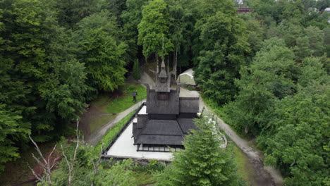 aerial view tilting over forest revealing a stave church in cloudy fantoft, norway