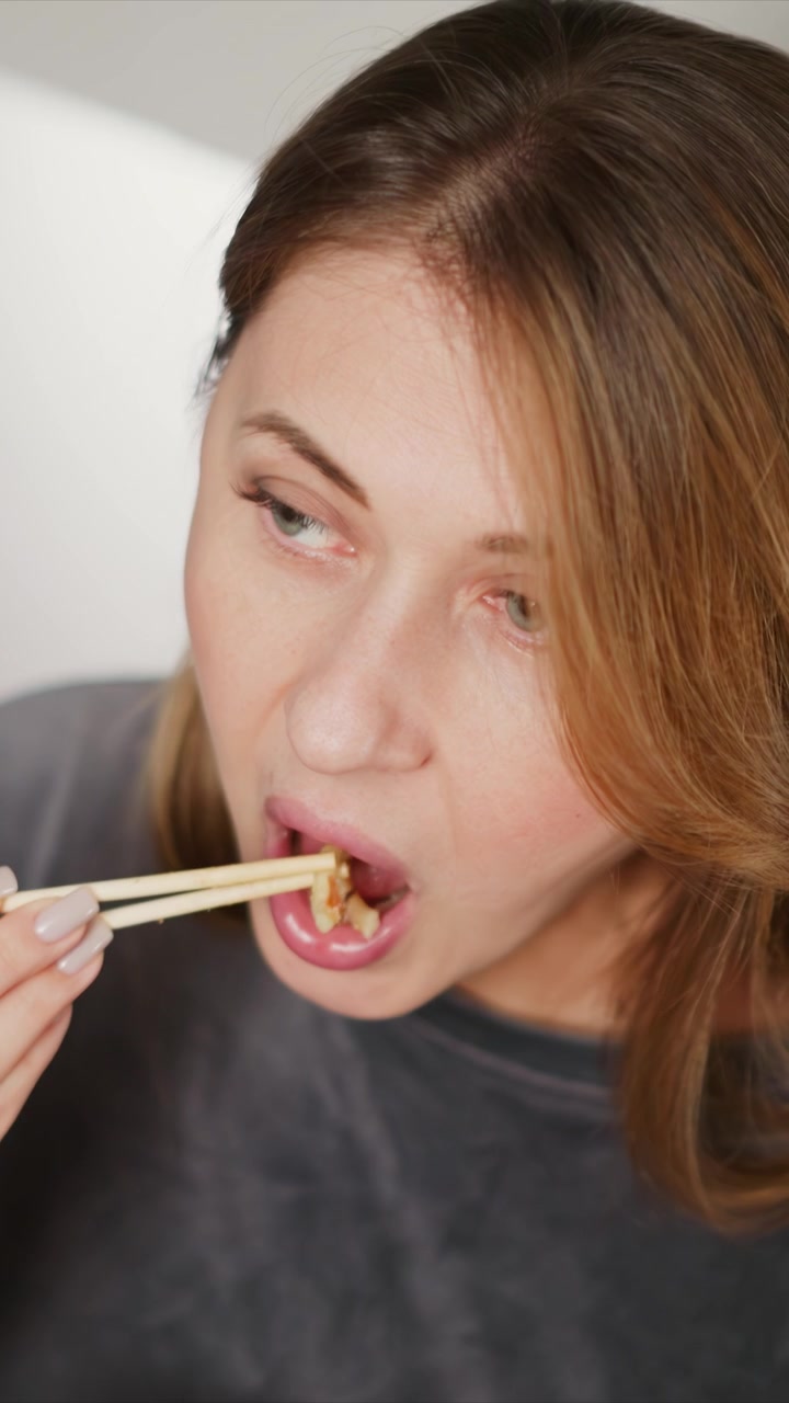 Close up of woman using chopsticks to eat food. woman holds utensils near their mouth focusing on eating activity with soft lighting and plain background