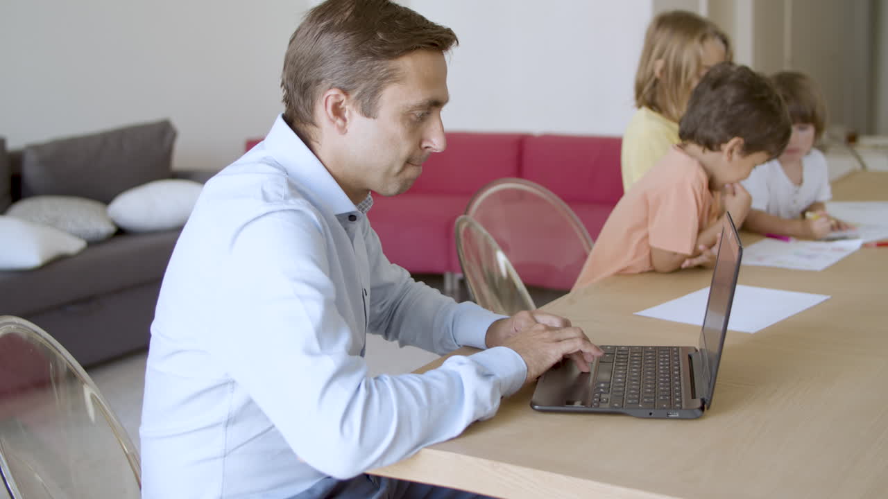 papá caucásico trabajando en una computadora portátil y niños lindos pintando garabates