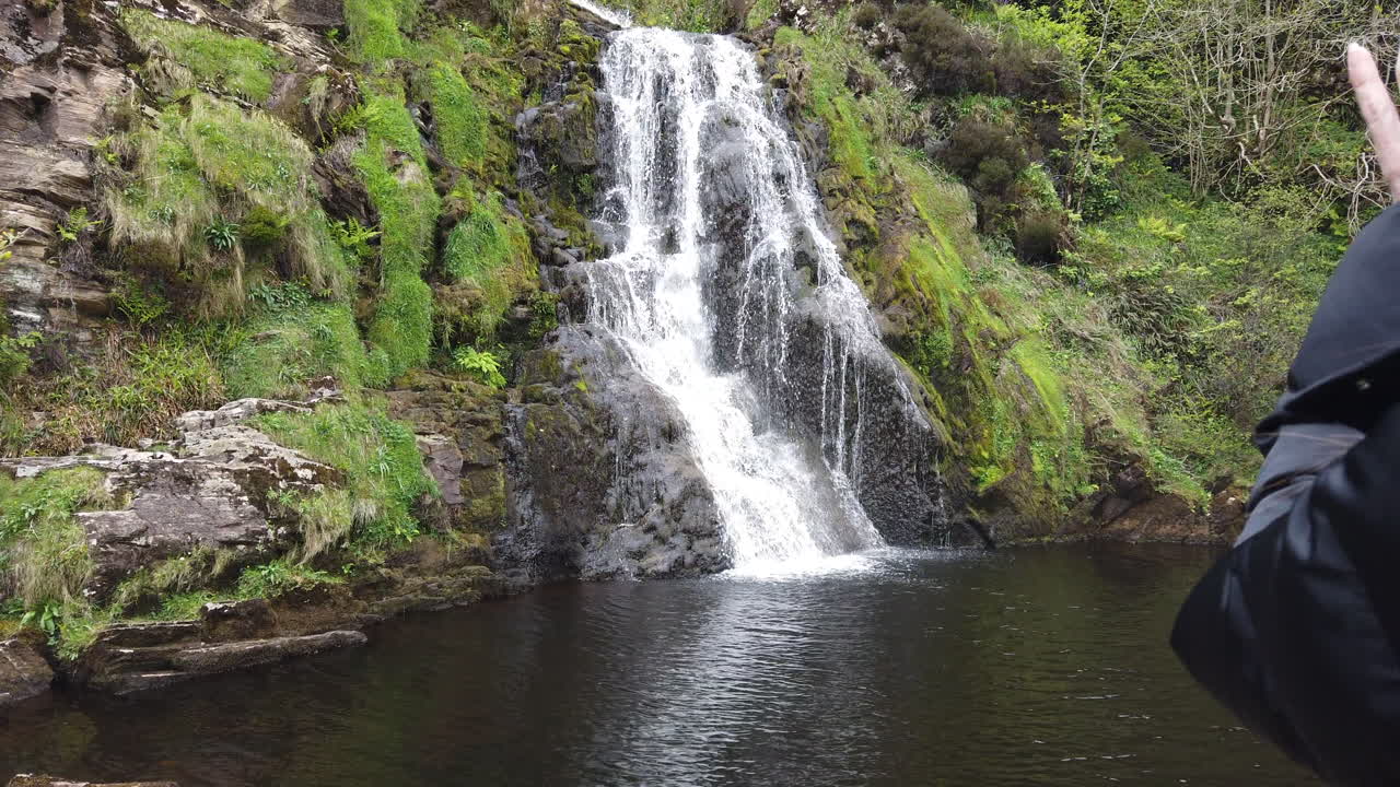 Professional photographer capturing stunning waterfall cascading through lush green irish countryside, documenting natural landscape during scenic outdoor journey