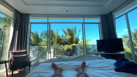 pov of wealthy individual on king-sized bed in luxurious room with open balcony and palm trees