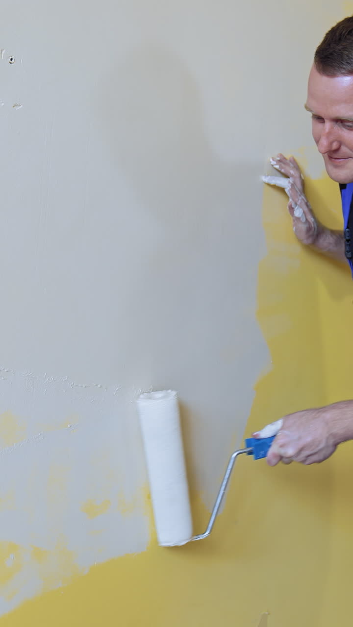 Man making repairs in new flat. Young man painting wall with roller brush while renovating his apartment. Vertical video