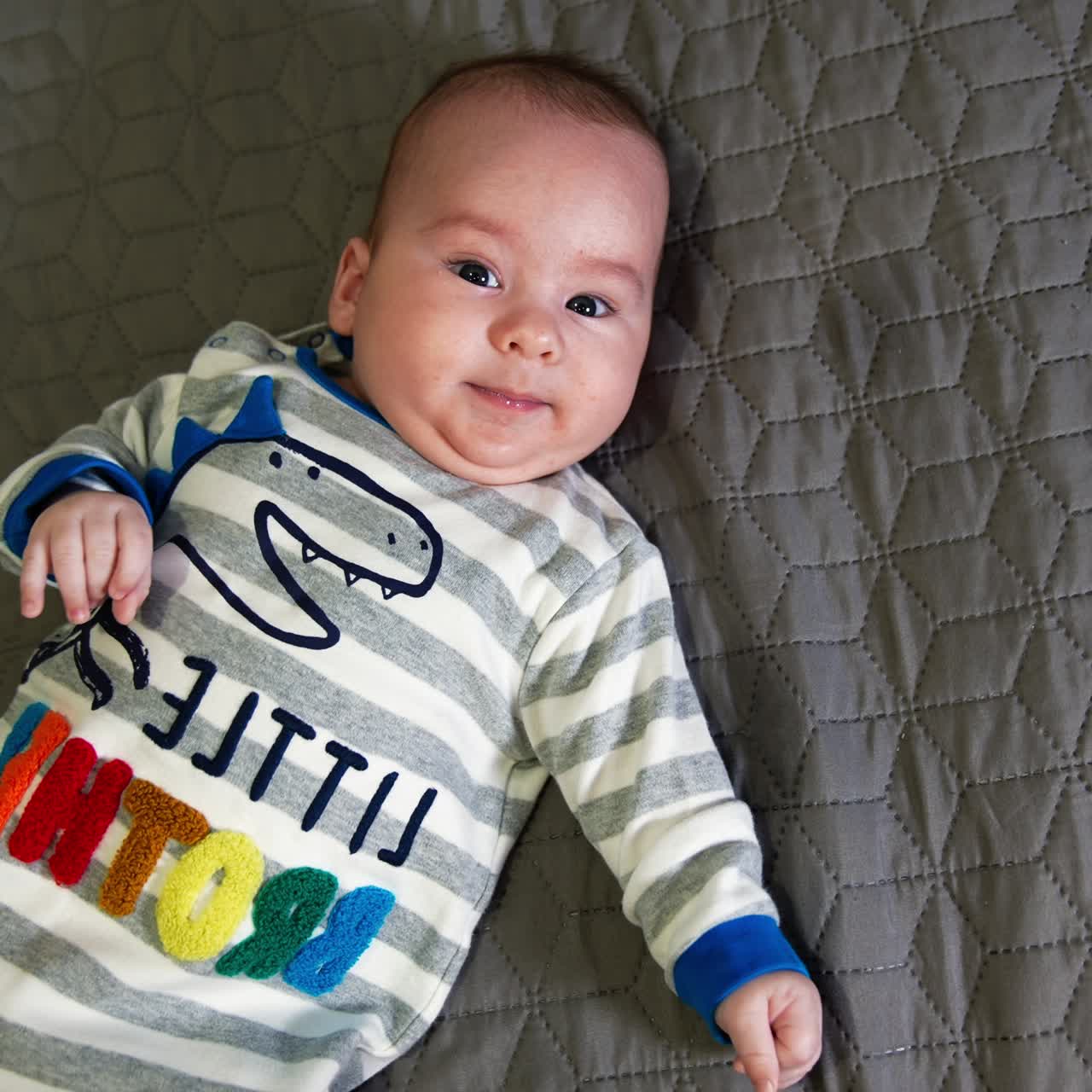 Anak laki-laki yang lucu berbaring telentang di ranjang besar. Bayi cantik mengenakan pakaian dengan tanda adik laki-laki. Close up. Tampilan atas.