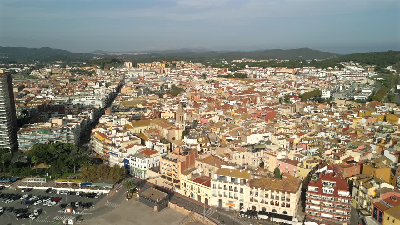Voo cinematográfico de drone em 4K sobre Palamós, Espanha, do porto e da praia em direção à cidade, inclinando-se para baixo para revelar uma igreja. Movimento suave para frente, vista aérea de uma vila costeira mediterrânea