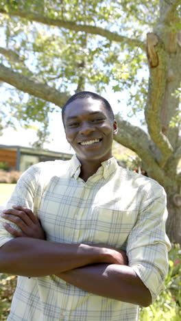 vertical video: smiling man standing outdoors with arms crossed under tree in park