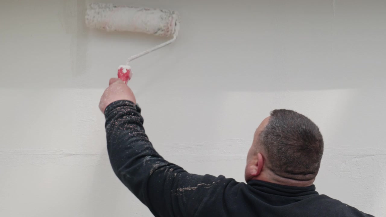 Worker painting a wall with a roller, renovation process in progress