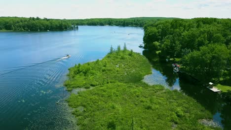 4k drone video of a lake canal in the summertime with a pontoon boat moving across the blue water on a sunny day in northern michigan in usa