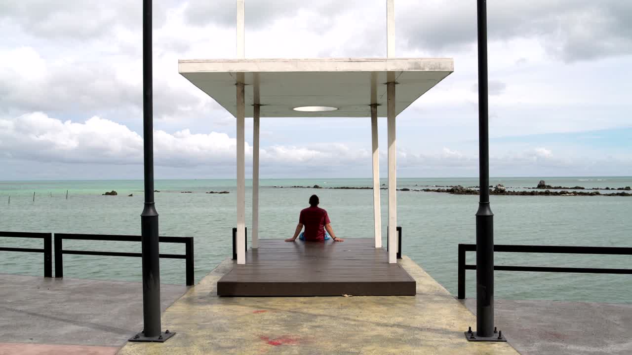 A man sits on a pier and looking at the sea