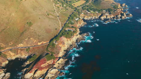 private mansions with lots of green trees located near the pacific ocean. rocky shore with car road from air perspective.