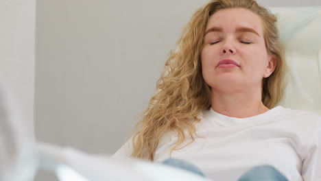 client in white top sits calmly on clinic chair with eyes closed in relaxed posture, appearing to gently open eyes under soft lighting, conveying peace and personal care atmosphere