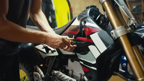 a male mechanic in a gray t-shirt disassembles a motorcycle using special tools. a man with sinewy arms works in his workshop