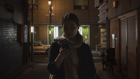 woman walking along dark city street at night using mobile phone