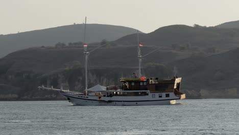 small tourist boat cruises the ocean against the backdrop of a mountain on komodo island