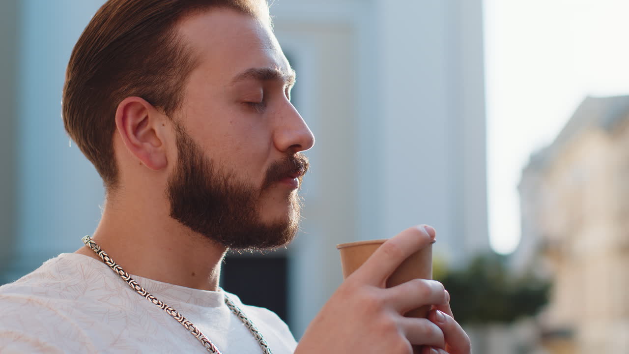 Young man guy enjoying drinking morning coffee hot drink relaxing taking a break in city street