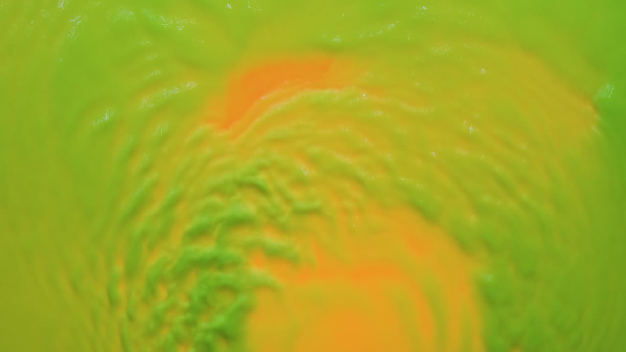 ondas abstractas de pintura de neón verde sobre un fondo naranja. vista desde arriba.