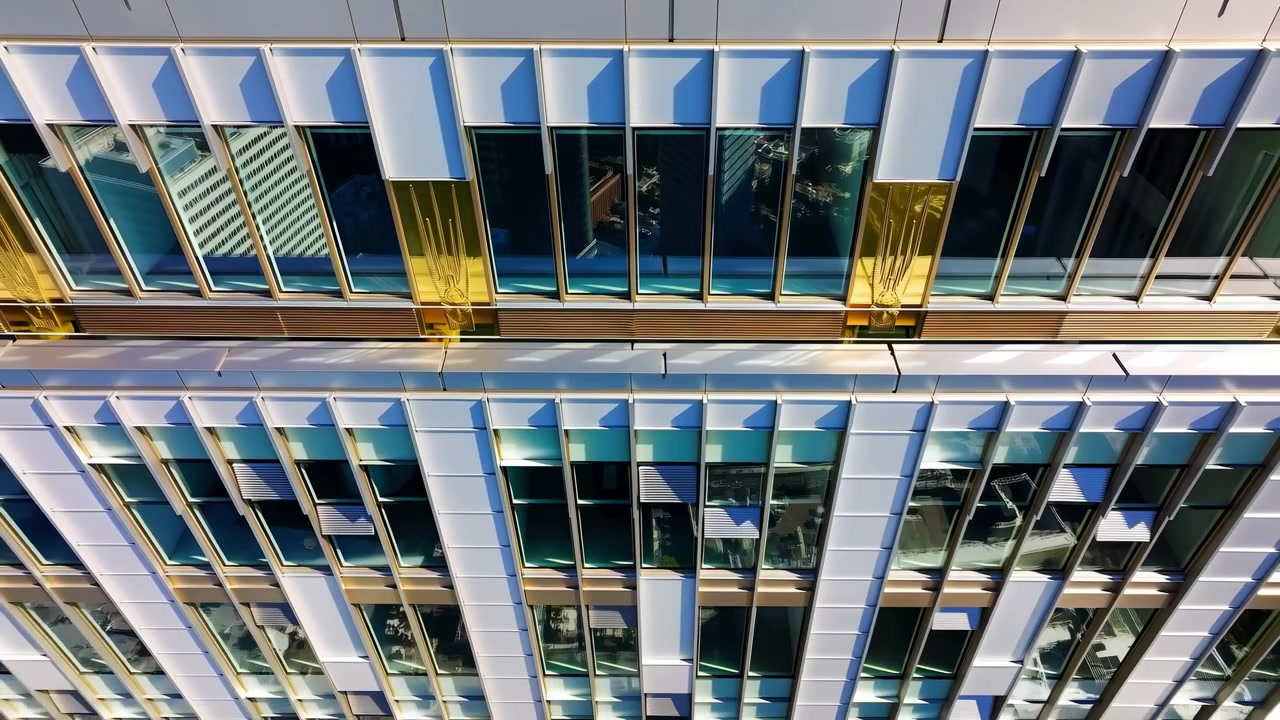 Vista simétrica de la fachada de una moderna oficina de gran altura con paneles de ventanas de vidrio reflectante, patrón de cuadrícula geométrica y coloridos reflejos de luz.