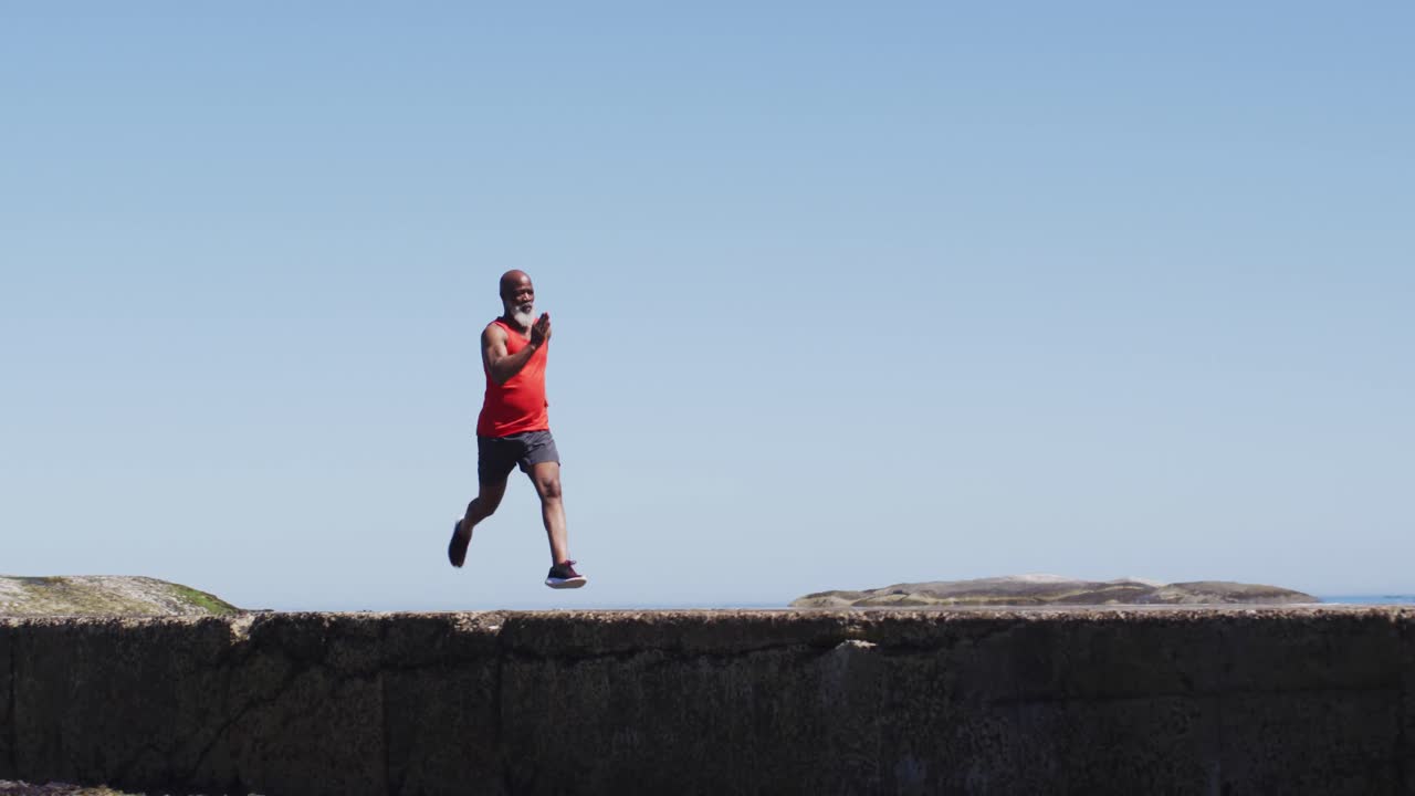 hombre afroamericano senior haciendo ejercicio corriendo sobre rocas junto al mar