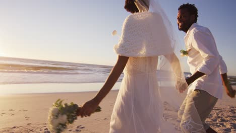 african american couple in love getting married, holding hands on the beach at sunset