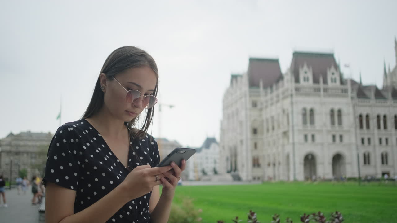 joven usando un teléfono inteligente frente al edificio del parlamento húngaro