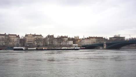 Ruhige-Rhone-Und-Ein-Frachtschiff,-Das-Unter-Der-Gewölbten-Stahlbrücke-Von-Lyon-Vorbeifährt-Und-Den-Alten-Europäischen-Charme-Zur-Schau-Stellt