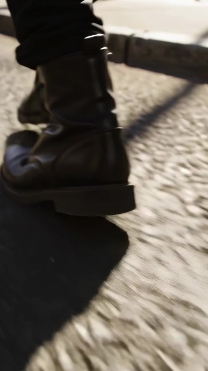 Video verticale: Adulto con pantaloni scuri e stivali allacciati che cammina su strada per mantenere il passo.
