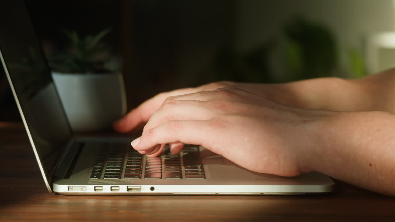 Primo piano di mani che digitano su una tastiera di laptop su una scrivania di legno.