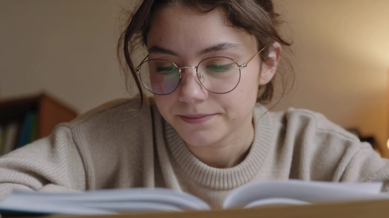 Leitor debruçado começando a ler um livro aberto no escritório em casa, de óculos, com suéter de tricô.