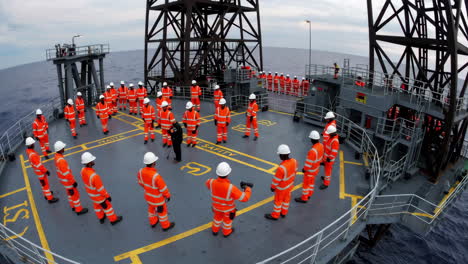 workers in orange safety gear gather for a safety briefing on an offshore oil rig