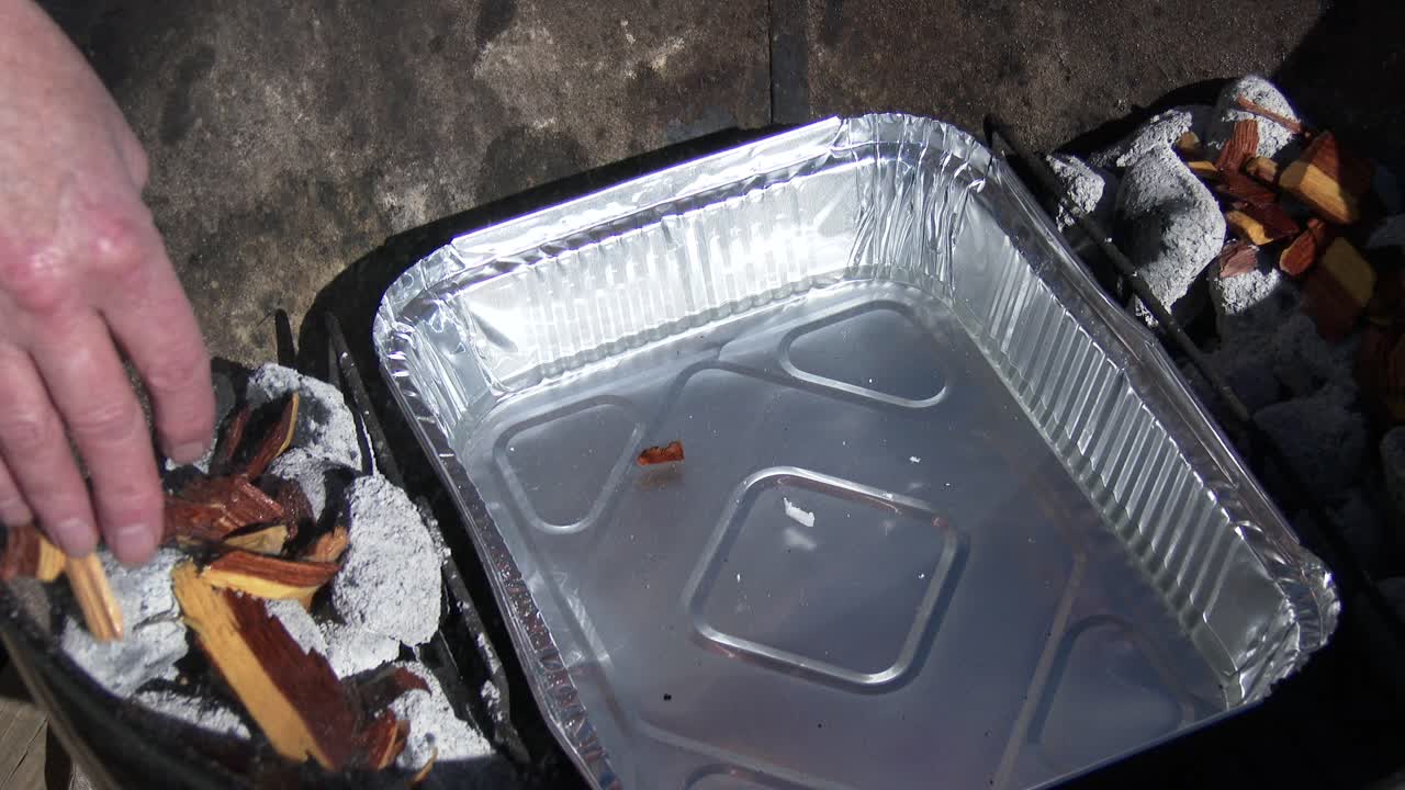 야외에서 사슴 고기를 훈제할 준비가 된 뜨거운 숯에 나무 조각을 놓습니다.