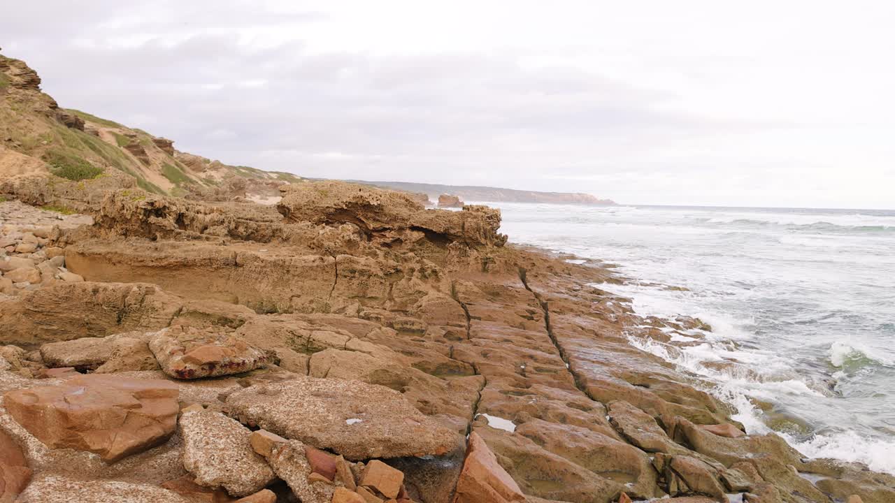 волны разбиваются на скалистом берегу, облачное небо