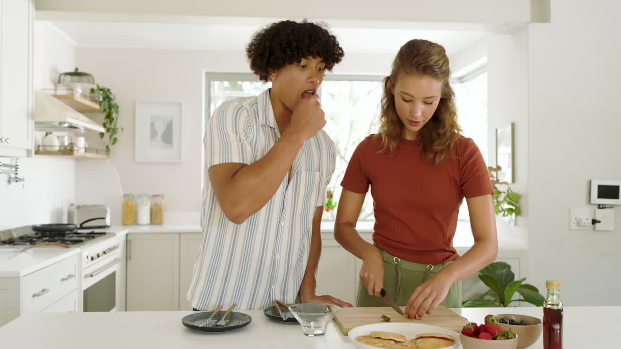 Diverse couple preparing breakfast together, slicing fresh strawberries in modern kitchen, at home