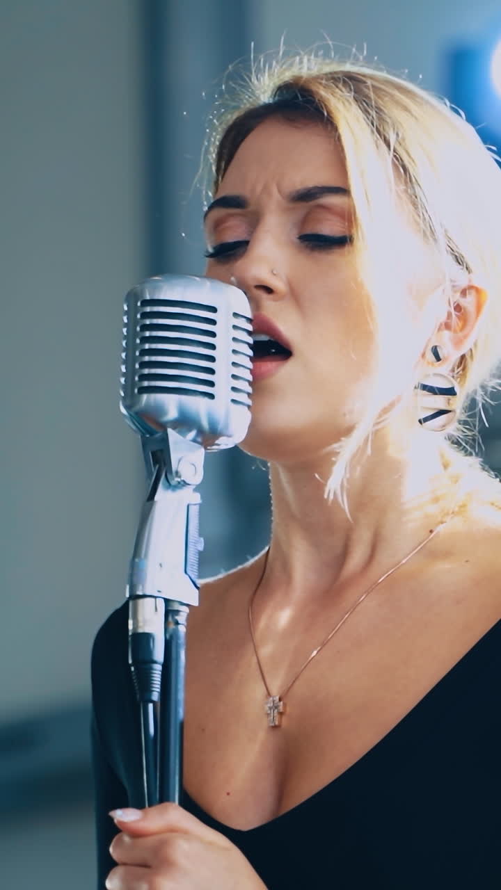 Blonde woman sings into the microphone. Attractive singer standing on the stage and singing a song. Musical entertainment. Vertical video