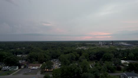 Aerial-drone-overview-shot-over-small-town-roads-and-parking-lot-with-driving-cars-at-sunset-surrounded-by-dense-vegetation