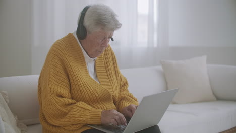 senior woman with gray hair make video call using laptop at home. elderly woman having a video call with family smiling and waving. covid 19 stay connected. online chatting with friends