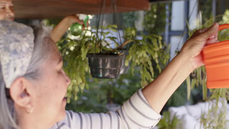 Happy-biracial-senior-couple-watering-hanging-plants-in-sunny-garden