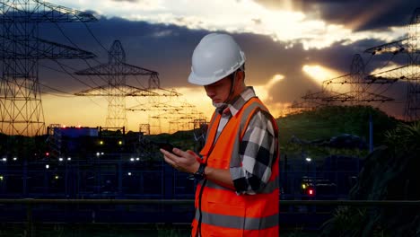 técnico de la línea de energía comprobando el teléfono inteligente al atardecer