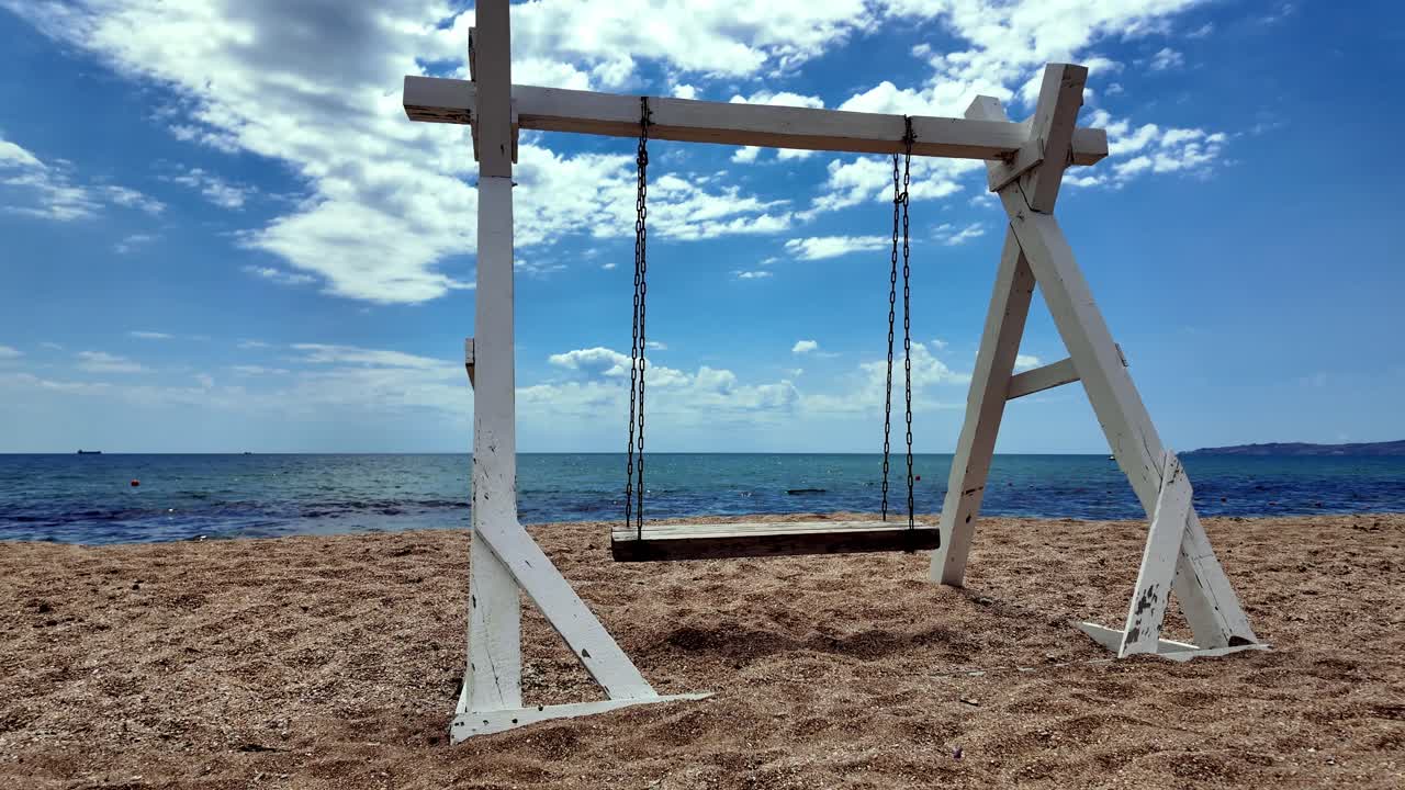 un columpio de madera blanca en una playa de arena en crimea con un cielo azul y el océano en el fondo
