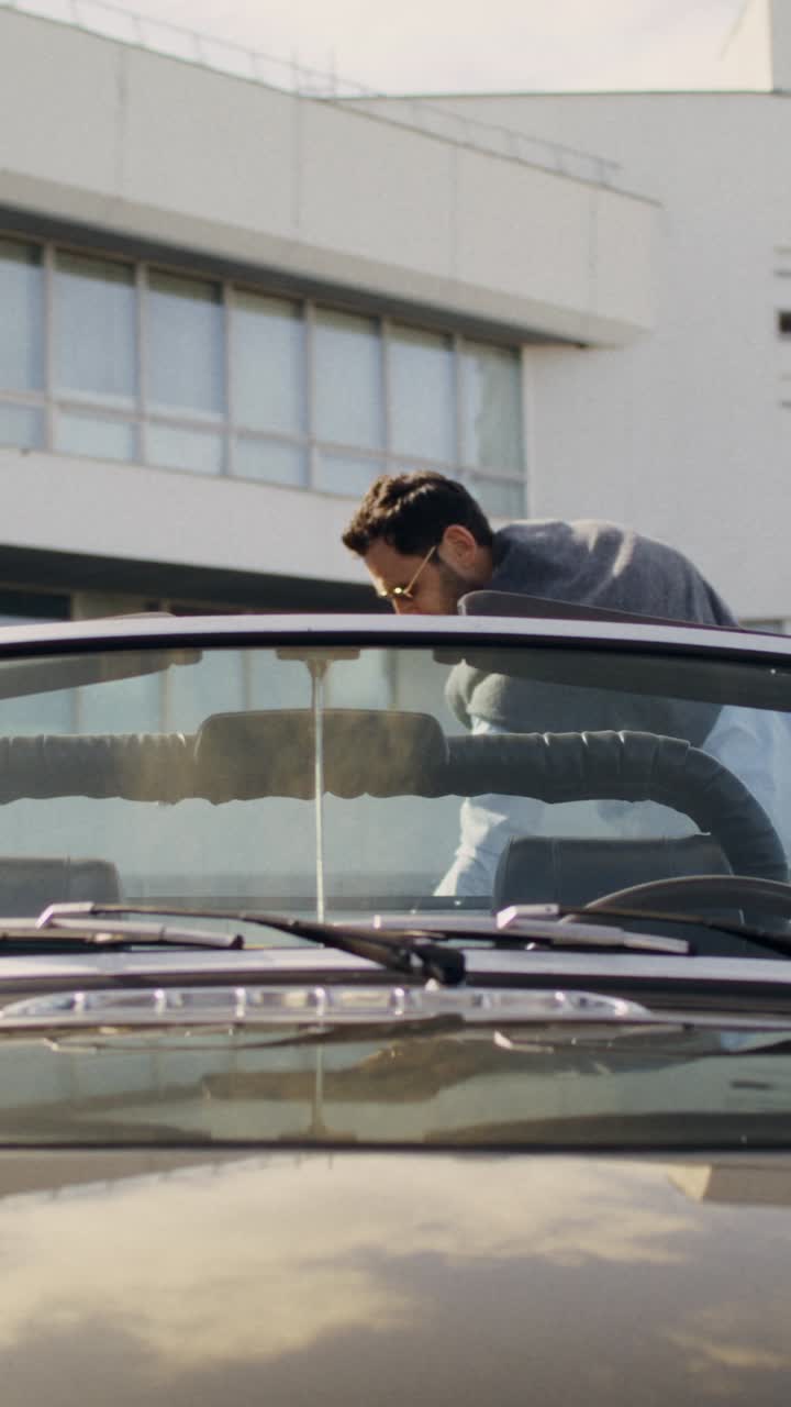People near a vintage convertible car near a modern building