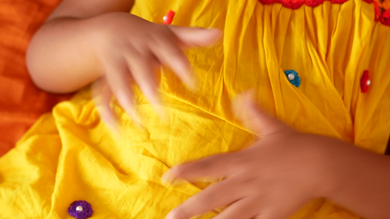 primer plano de las manos de una niña en un vestido amarillo con botones coloridos