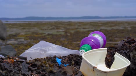 male tourist walking discards plastic bottle litter on and already polluted beach hills on the horizon