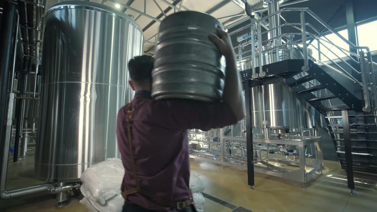 un joven cervecero con un delantal de cuero lleva un barril de cerveza artesanal en una cervecería moderna